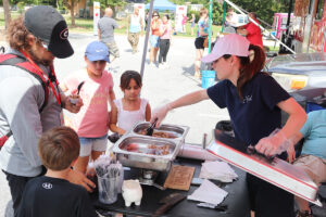 A woman serves barbeque samples to an adult and three kids at the 2021 Cook-off.